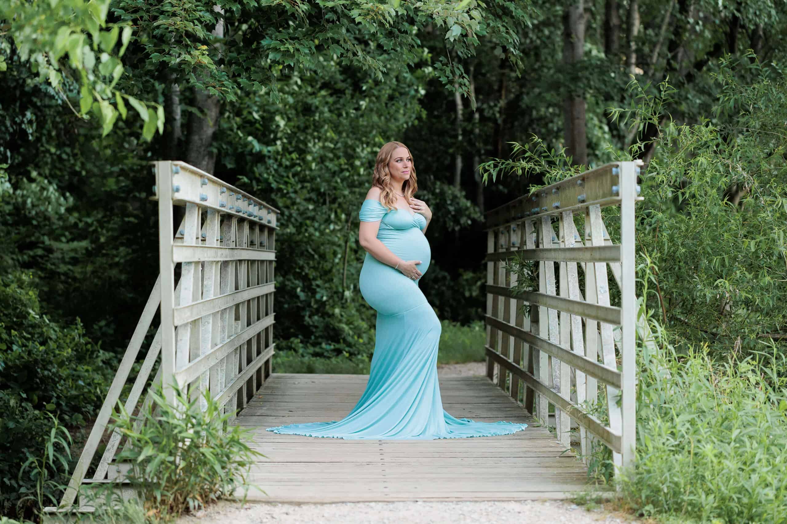 A pregnant woman on a bridge in a teal dress featured on a blog about Bellies and Babies Consignment.