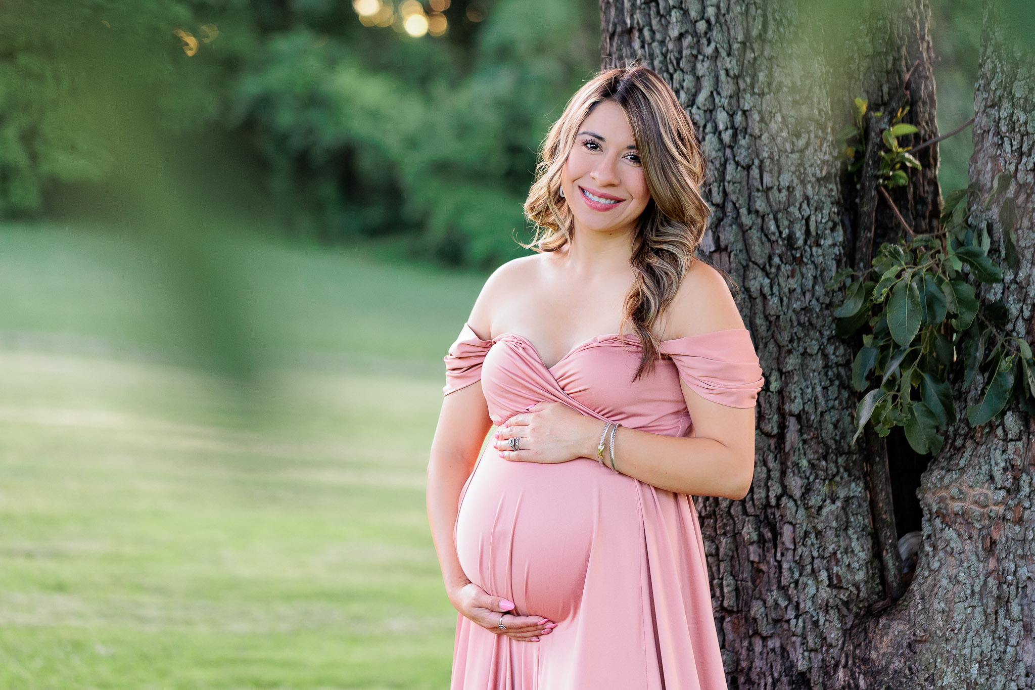 A mom-to-be wearing pink and leaning against a tree, featured in a blog about birthing centers in Northern VA