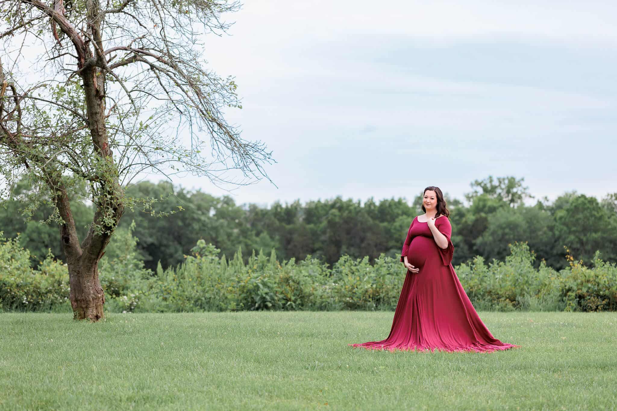 A blog about Centreville OB/GYN featuring a mother-to-be in a red dress standing in a field near a tree.