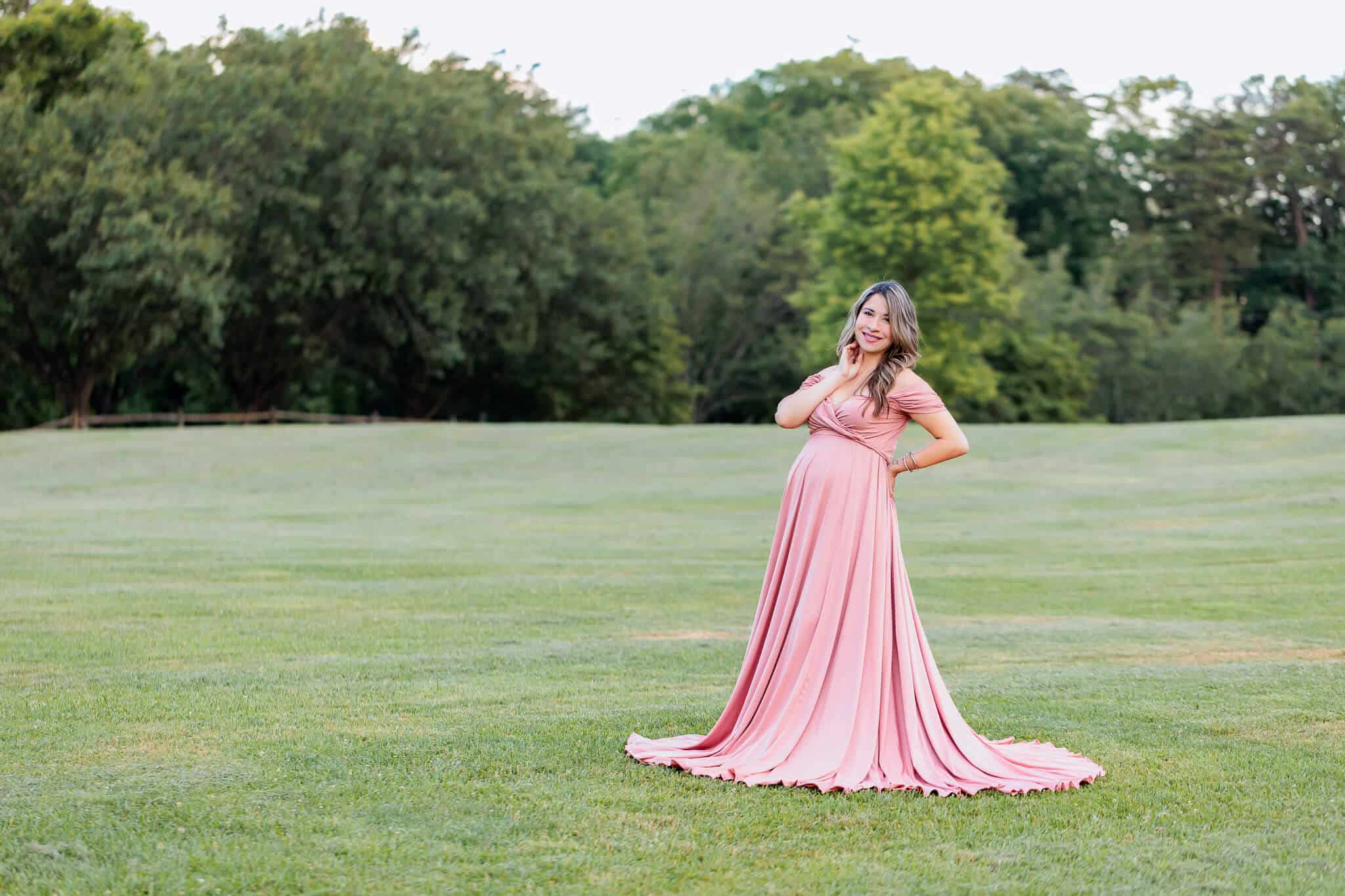 A beautiful pregnant woman posing in a pink dress in a field being featured on a blog about PediatriCare of Northern Virginia
