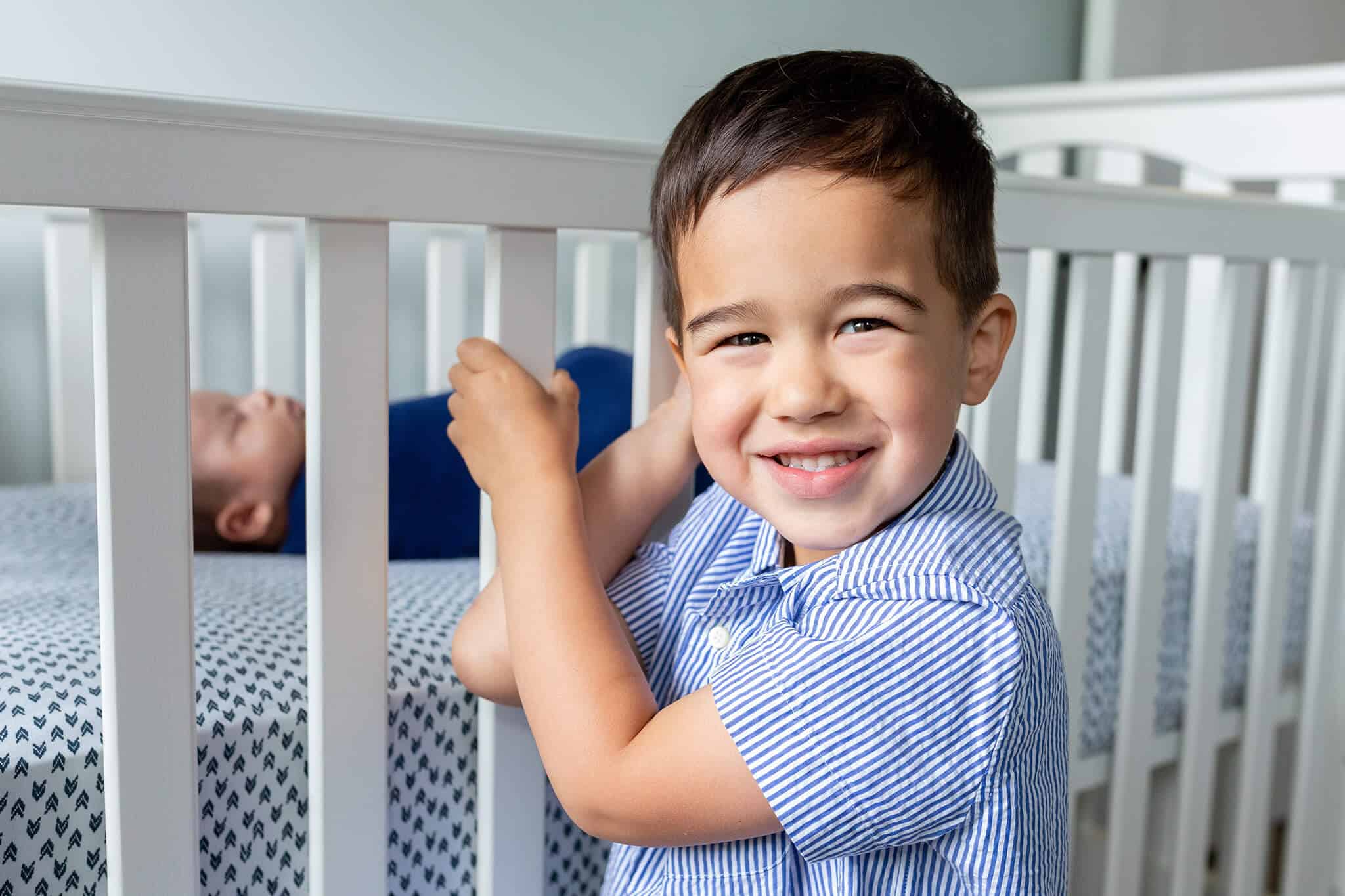 A blog about Pediatricare of Northern Virginia featuring a boy smiling at the camera and posing in front of his baby brother in a crib.