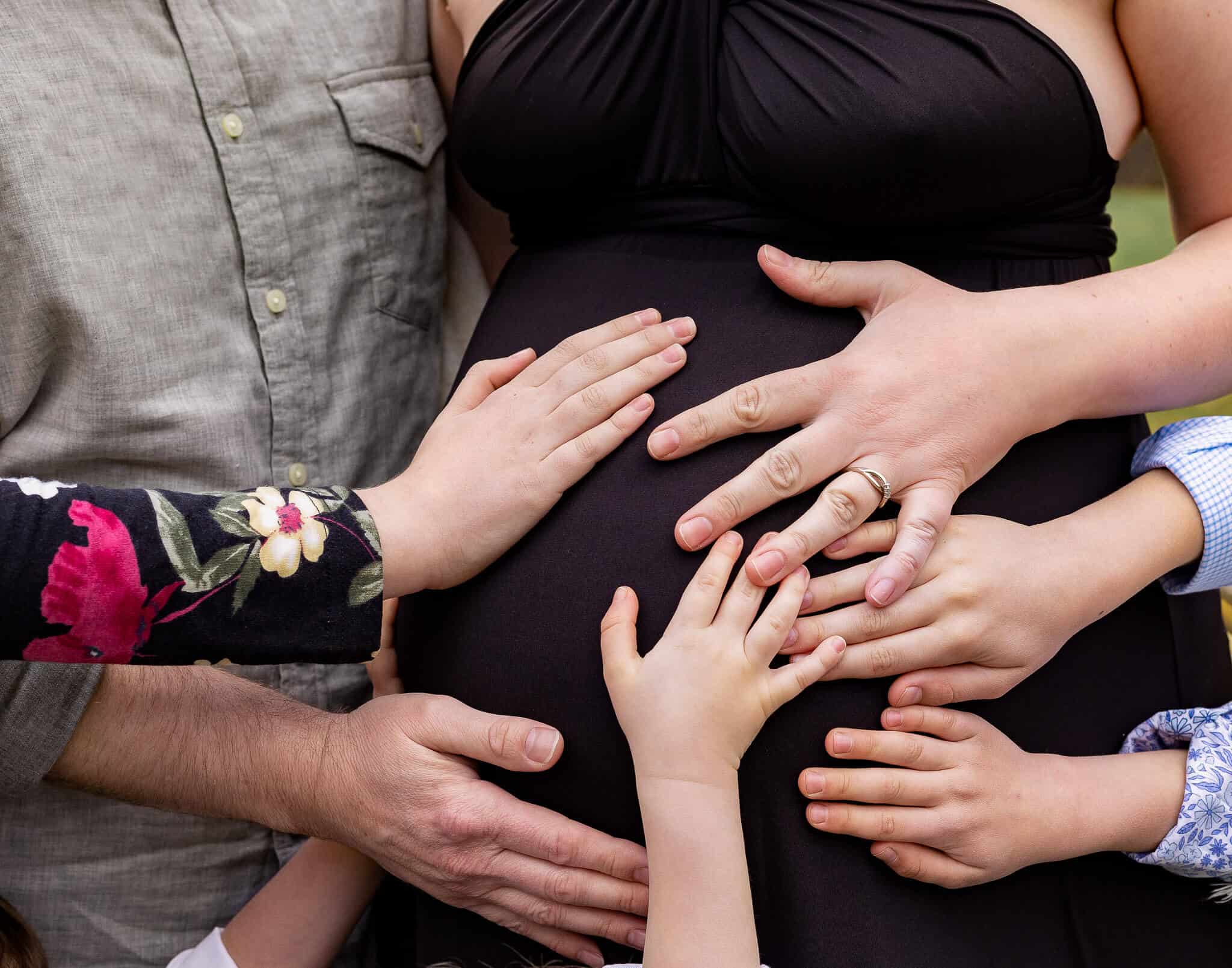 A blog about Physicians and Midwives Alexandria featuring a photo of a pregnant woman's belly with seven hands holding the belly.