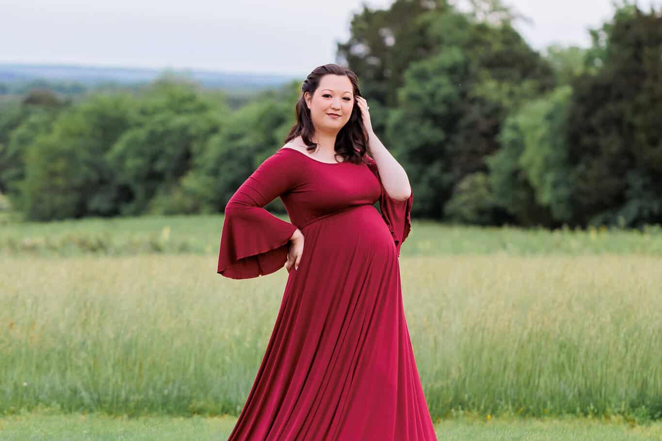 A blog about Postpartum Support Virginia featuring a photo of a pregnant woman with brown hair posing and a red dress in a field.