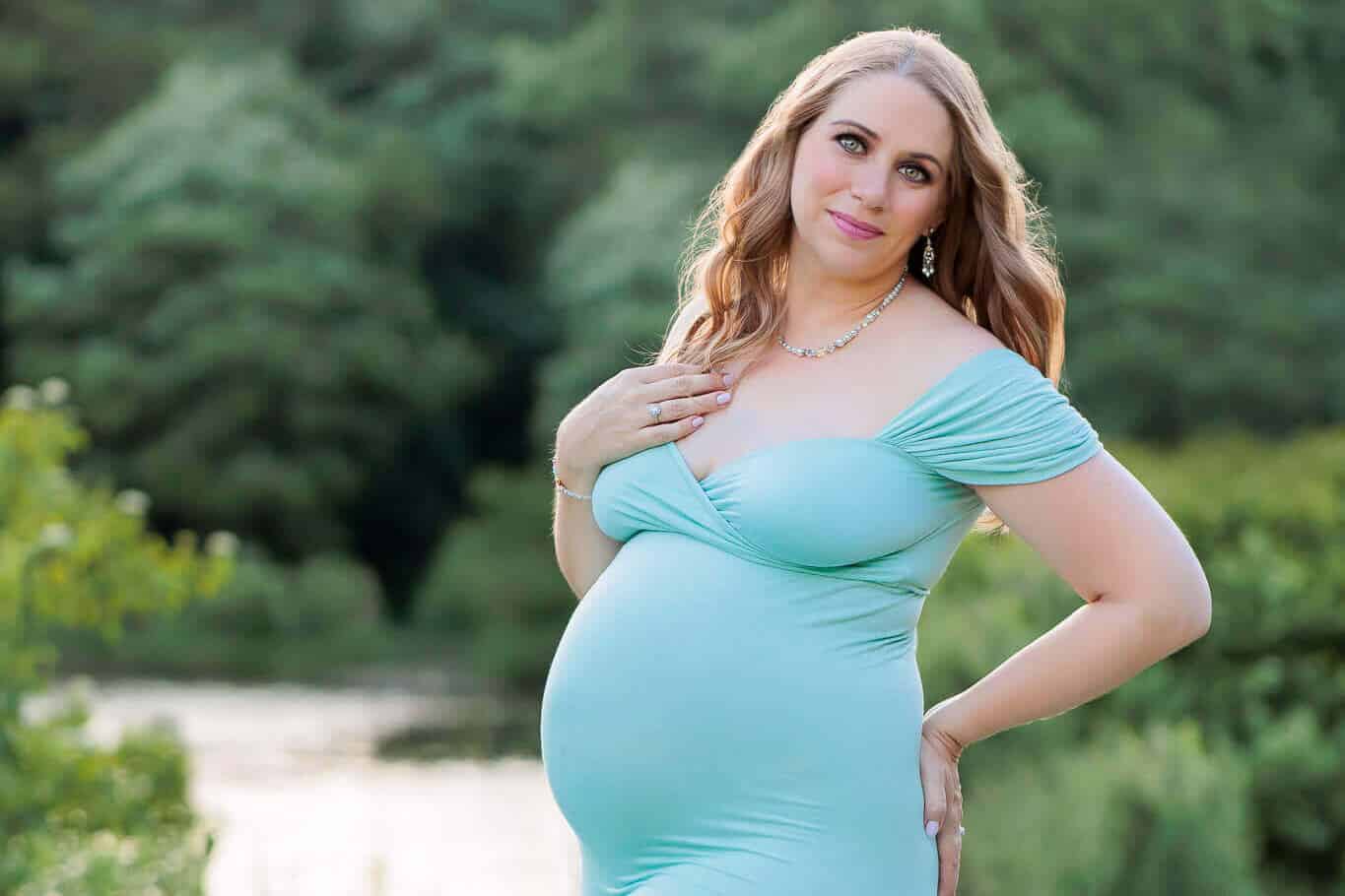 A pregnant woman in a teal dress posing in front of a lake featured on a blog post about Loudoun OBGYN.