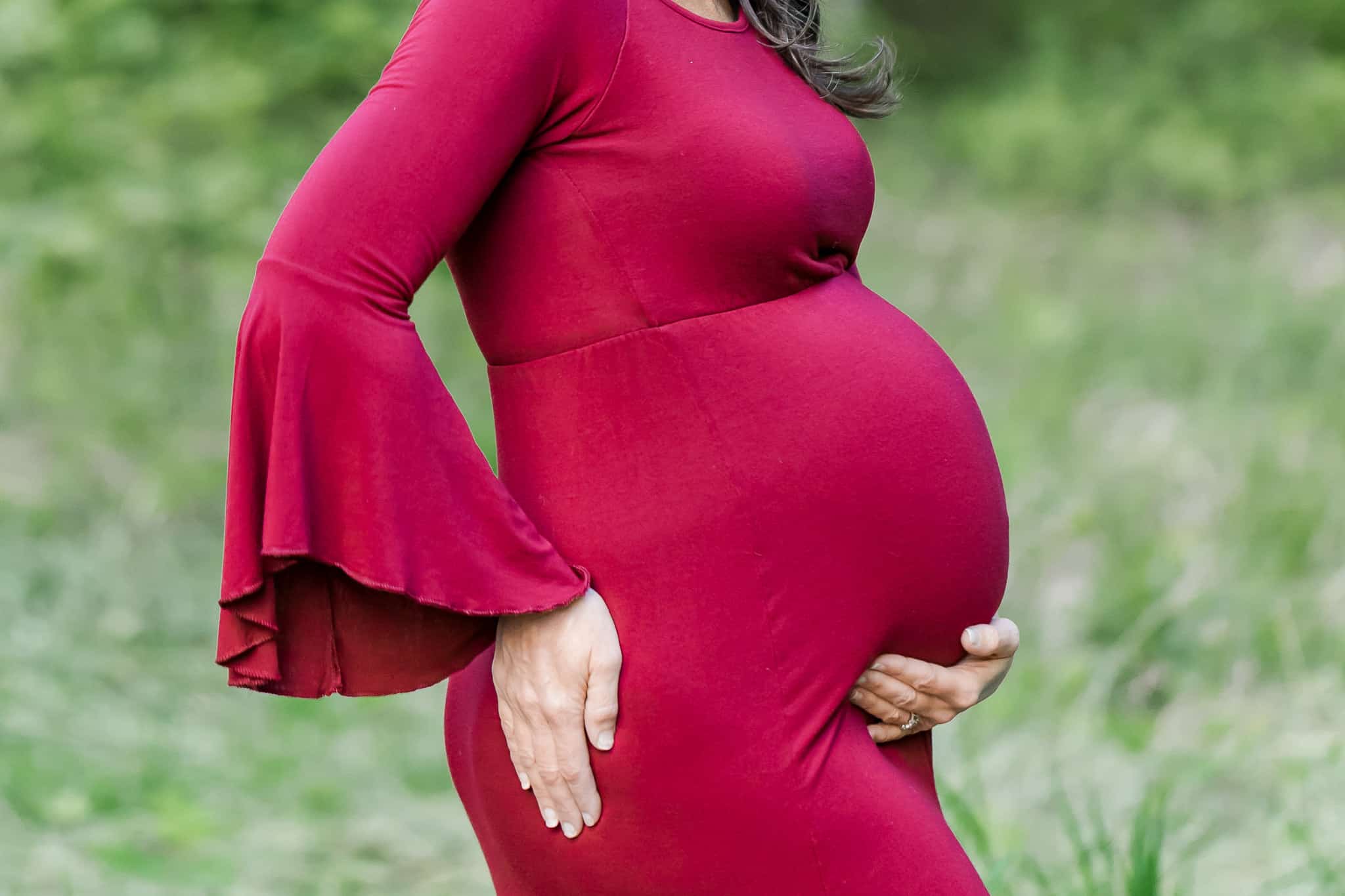 A closeup of a pregnant woman posing with her hand under her belly and on her hip being featured on a blog about Alexandria midwives.