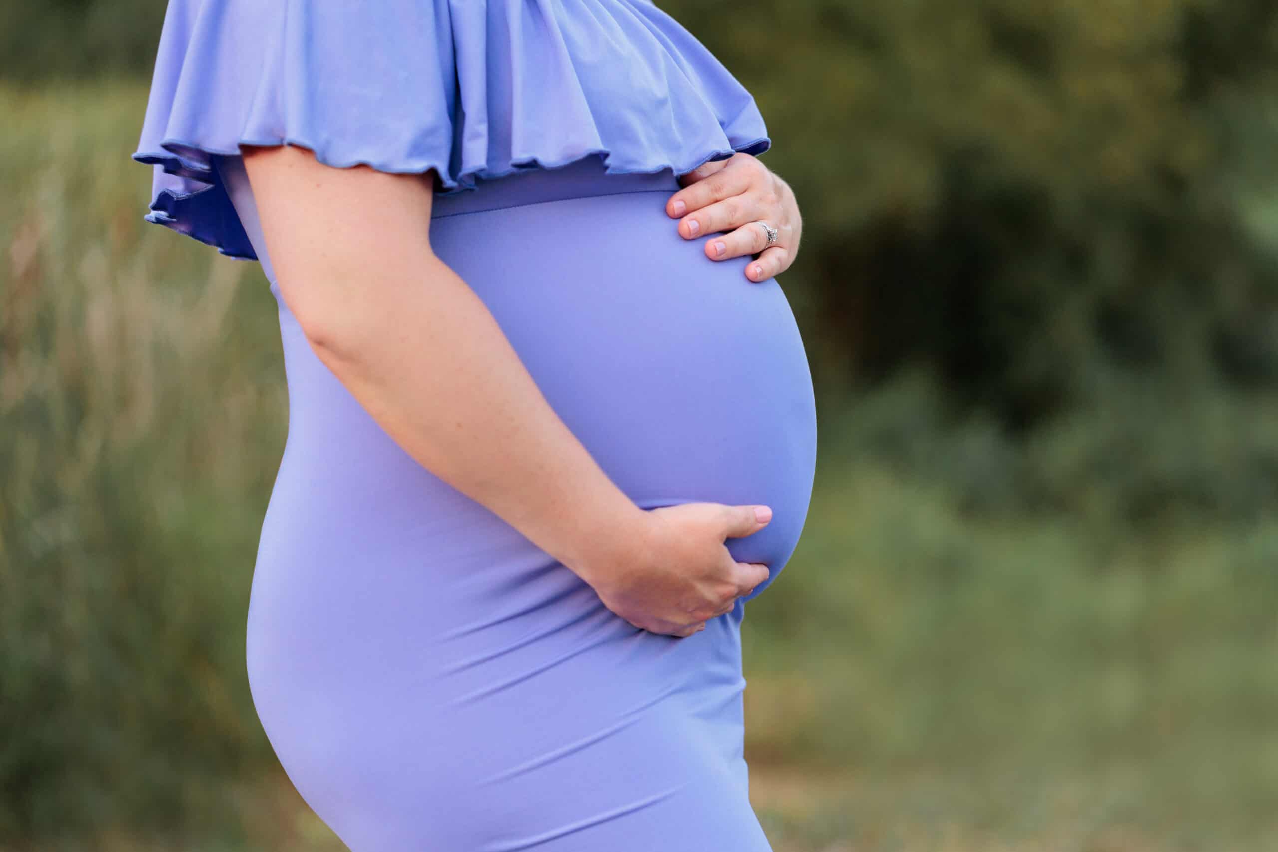 A closeup of a pregnant woman's belly in a purple dress being featured on a blog about Alexandria Women's Health Clinic.