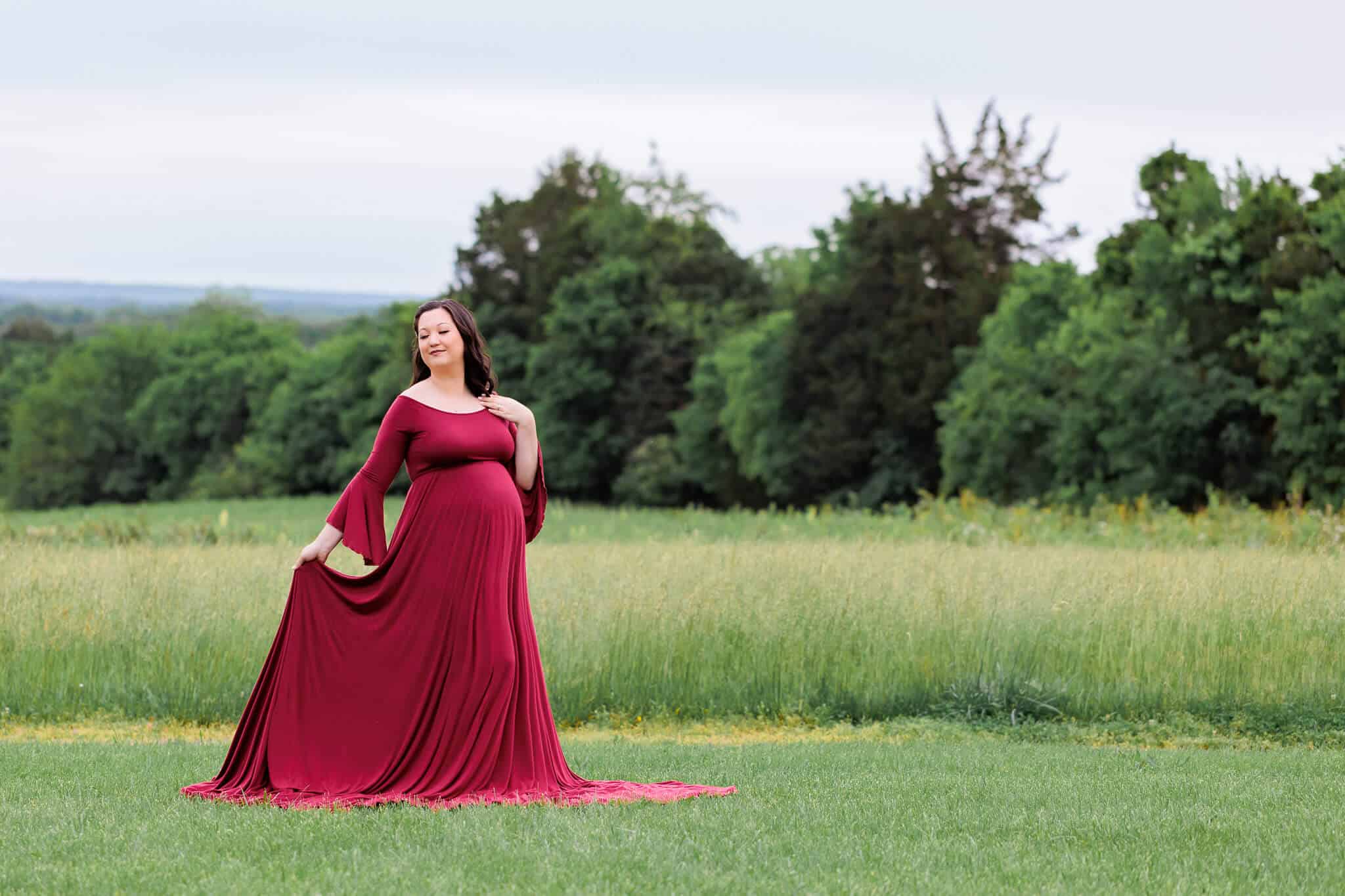 A mom-to-be in a field wearing a red dress and holding her train behind her, featured on a blog about Fairfax Home Birth.