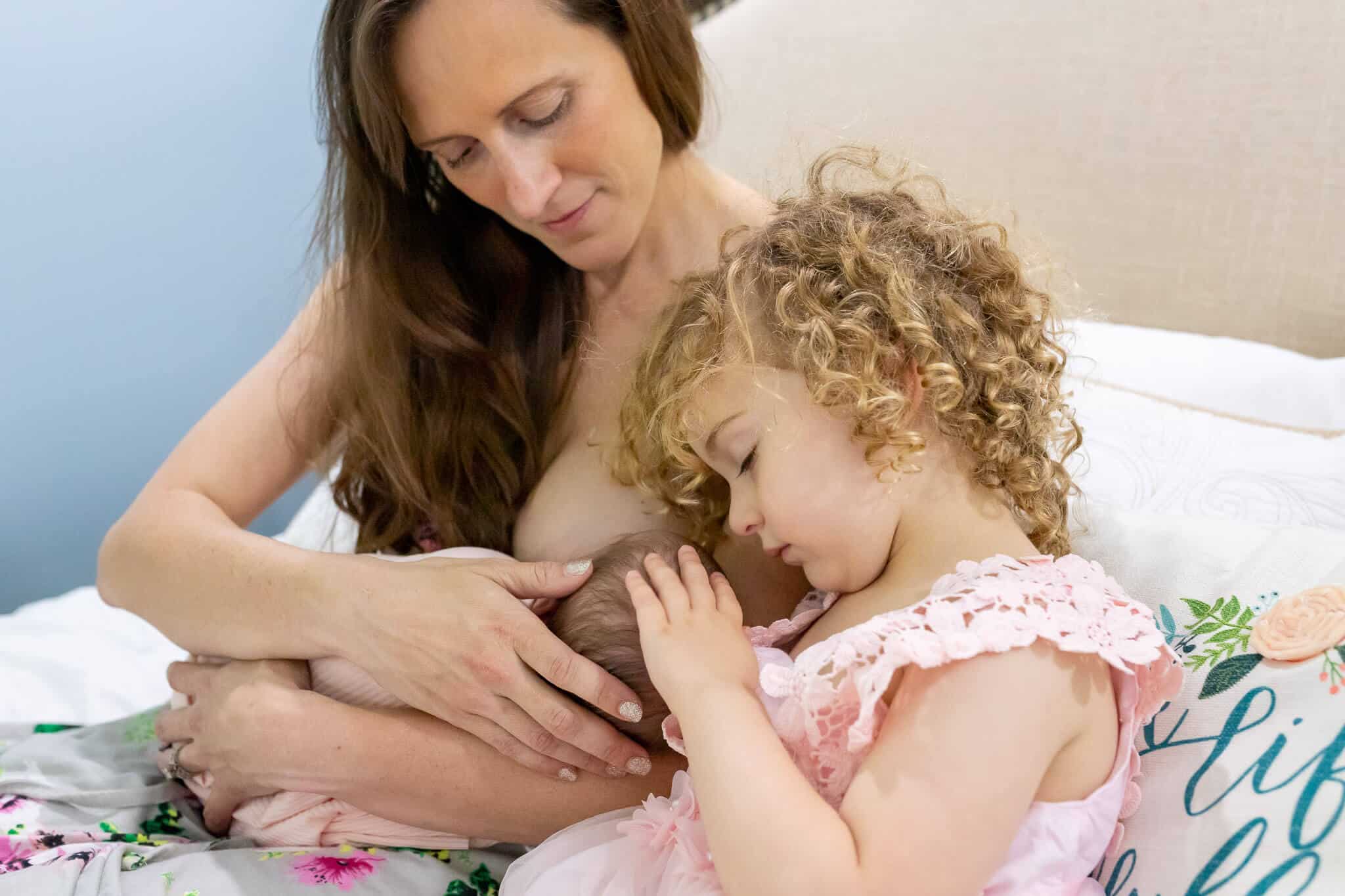 A mom breastfeeding her baby while big sister snuggles with them featured on a blog about La Leche League Northern Virginia.