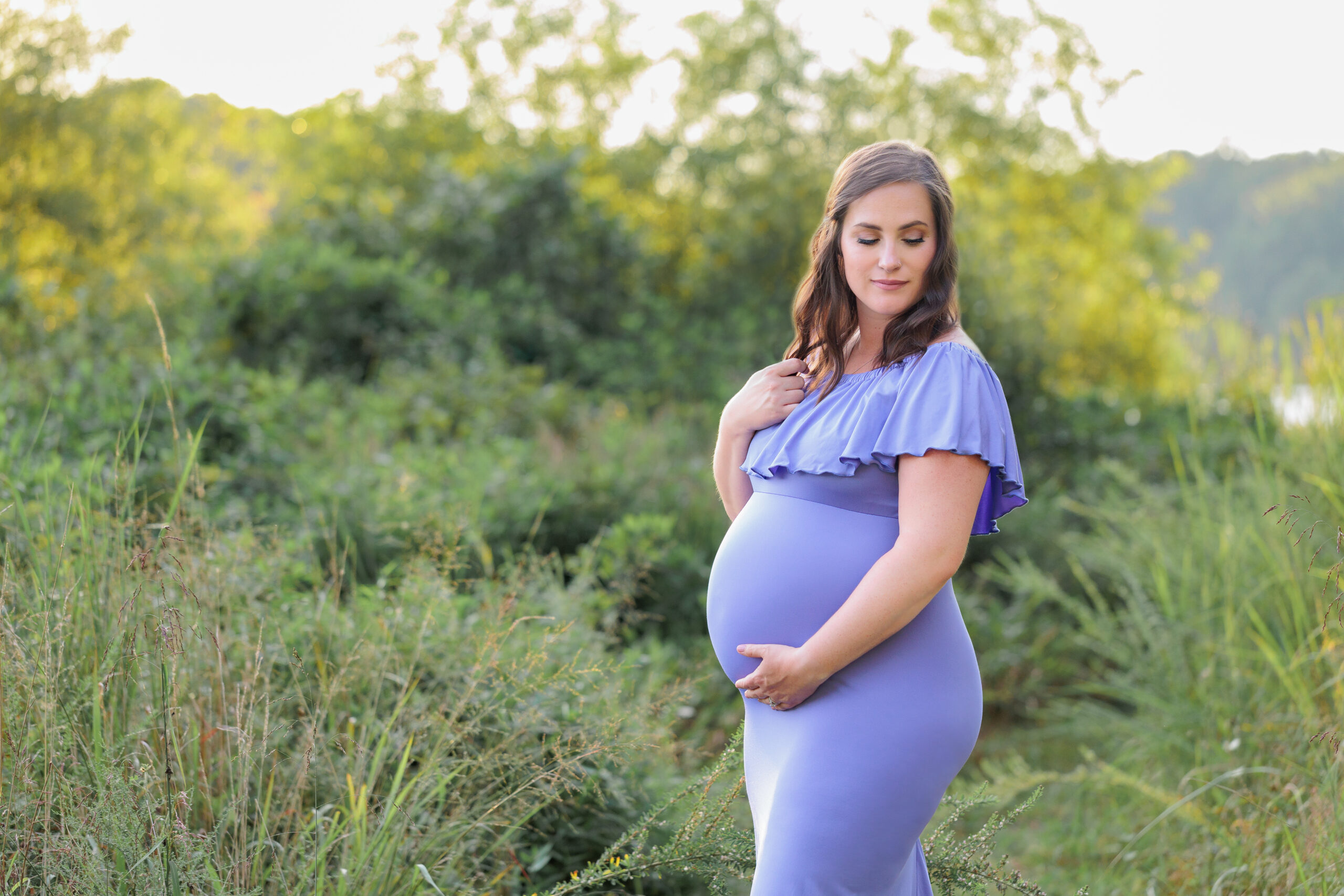 A mother-to-be wearing a purple gown and posing in front of green bushes, being featured on a blog about Lemon Lane Consignment.