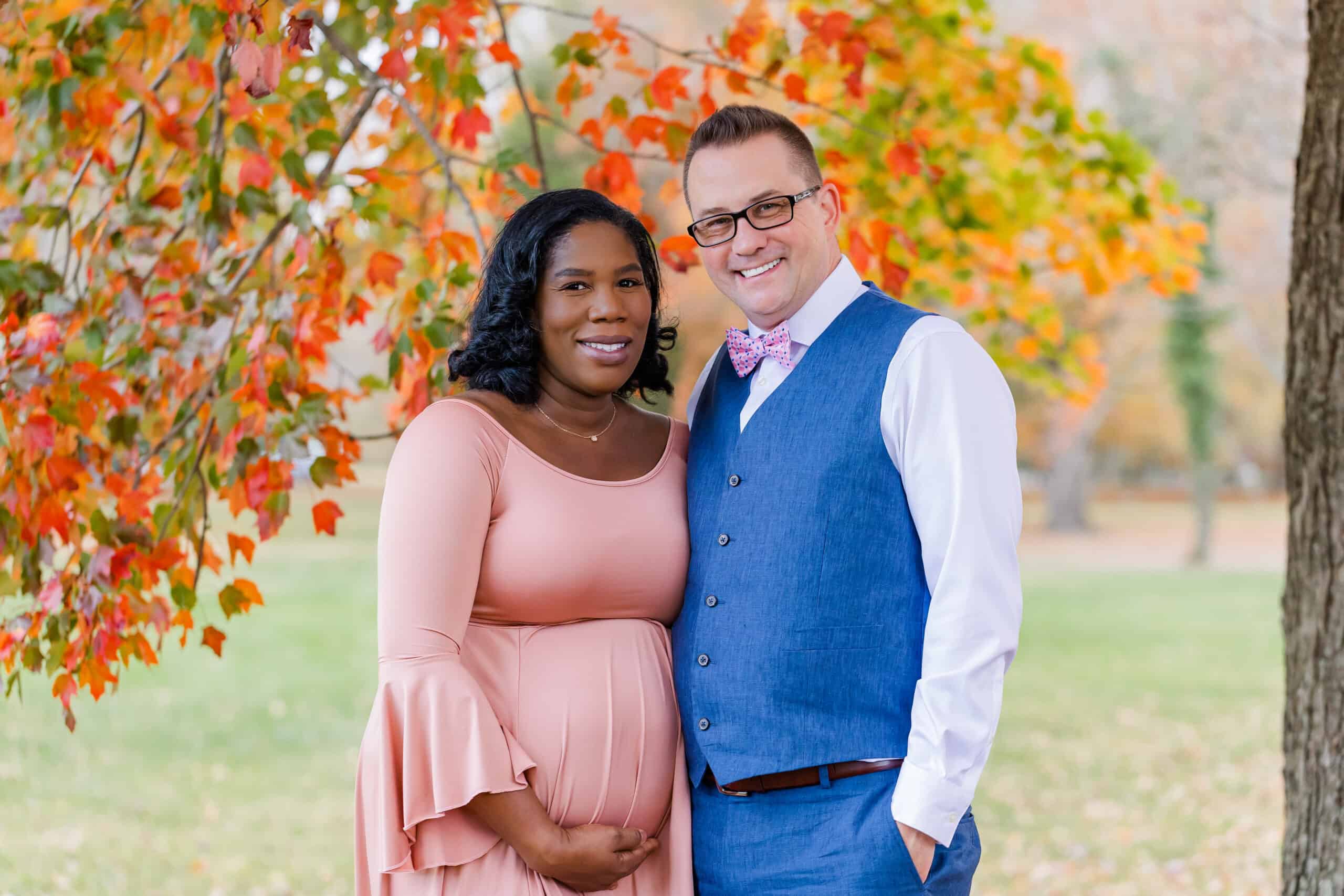 An expecting couple posing in front of fall foliage featured on a blog about Transition Physical Therapy.