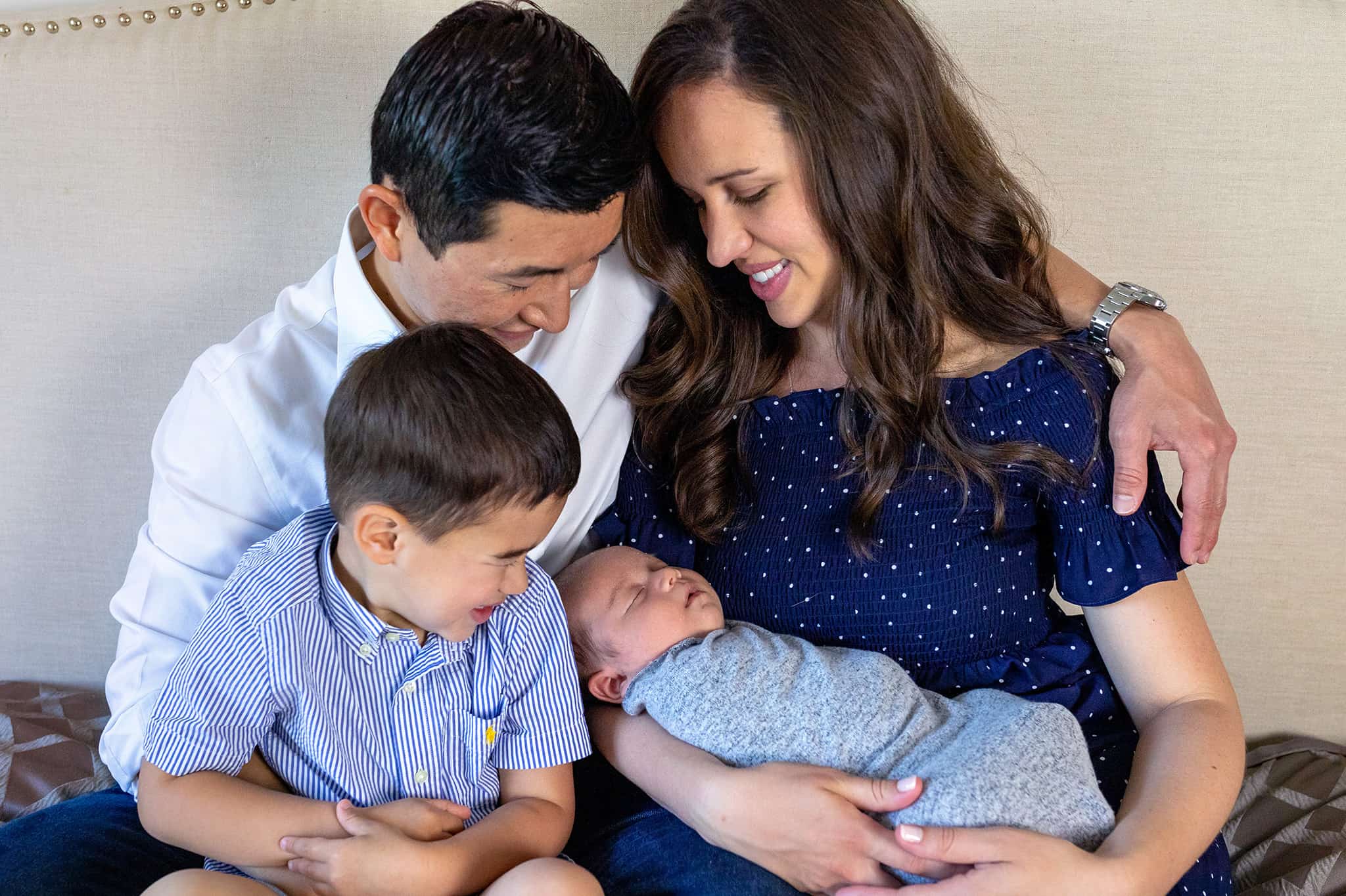 A family of four snuggling on their bed with a newborn boy featured on a blog about Thrive Breastfeeding.