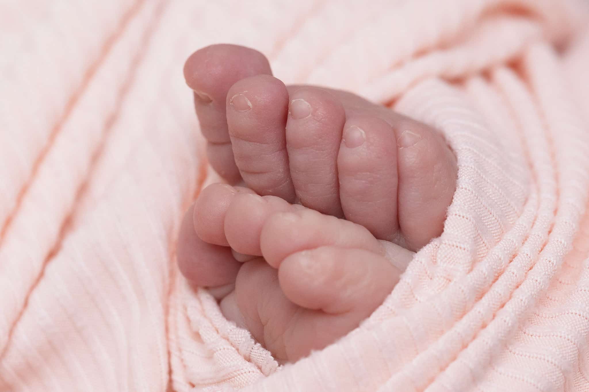 A close-up of a baby girl's toes wrapped in a pink swaddle.