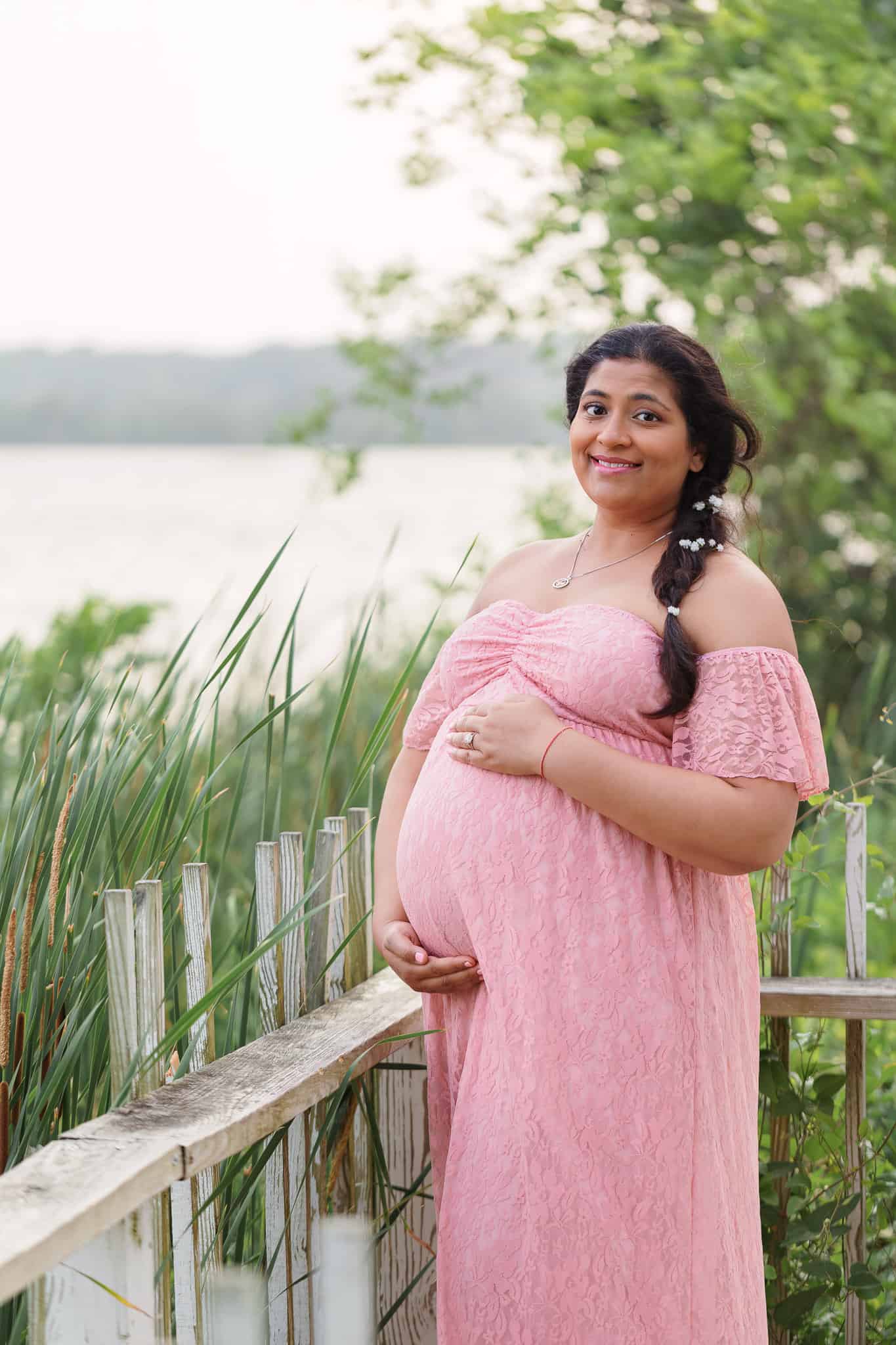 A pregnant mom in a pink dress posing among the reeds along the Potomac River.