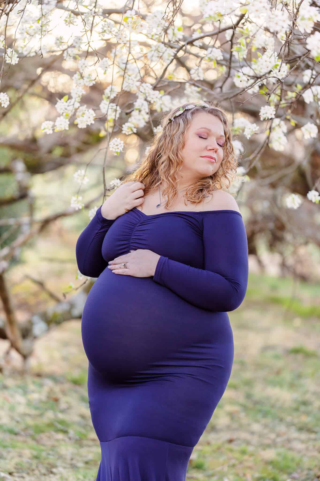 A mom-to-be posing under white blossoms at a Fairfax County park.