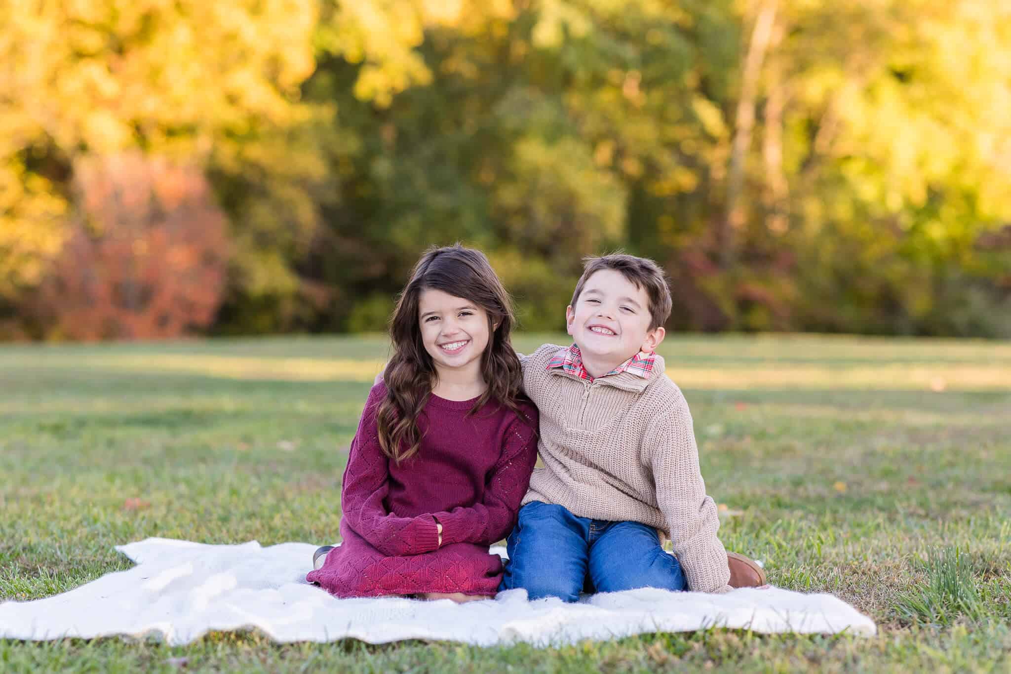 A brother and sister snuggling on a blanket in a field in the fall, featured on a blog about The Purple Goose.