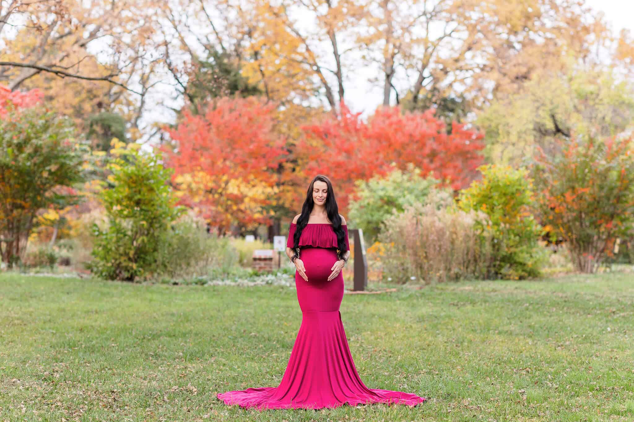 A pregnant woman in a red dress posing in front of beautiful fall foliage, featured on a blog about VHC Health.