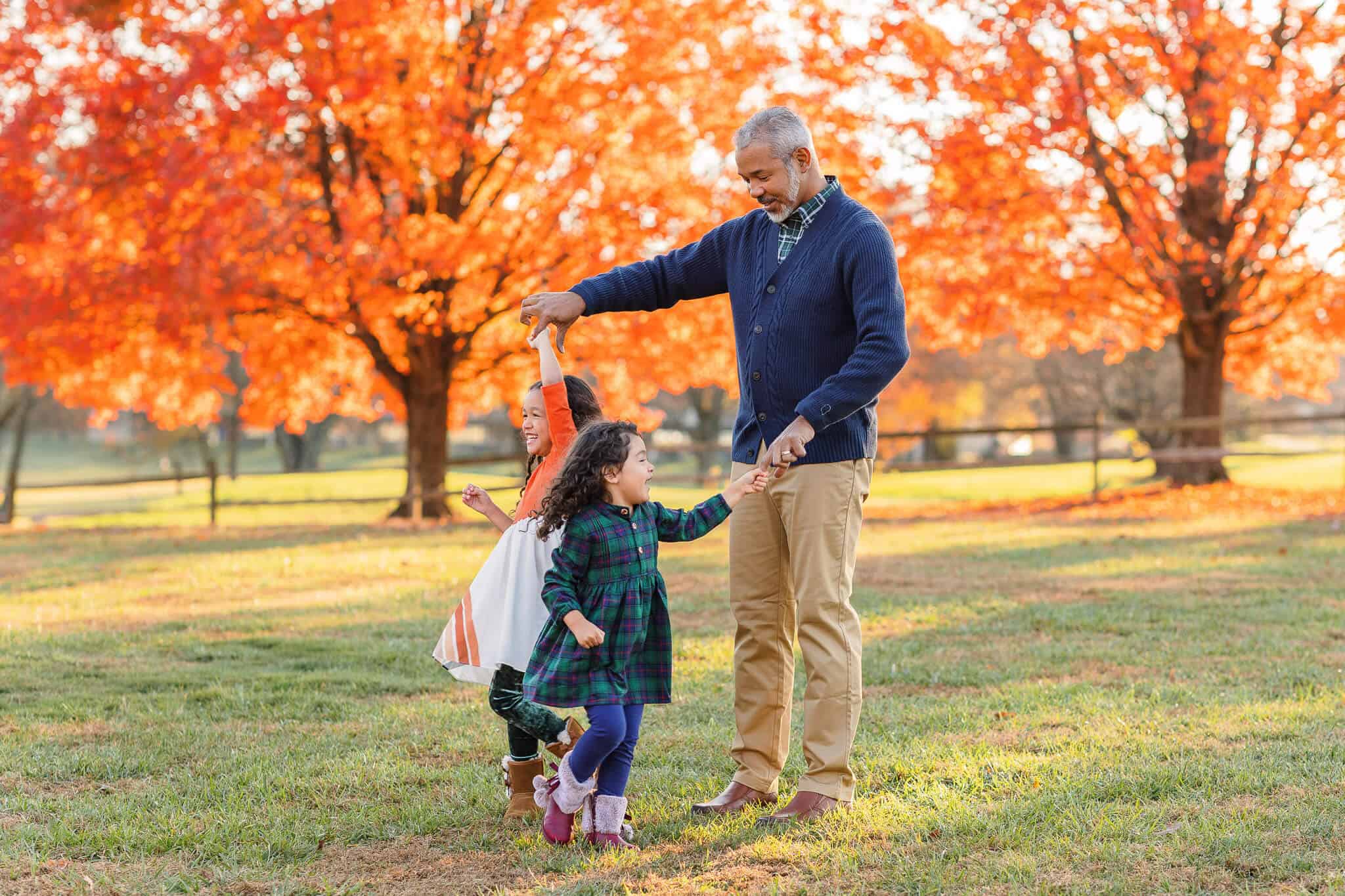 A dad twirling his daughters in a field with beautiful orange trees in the background, featured on a blog about Scramble Alexandria.