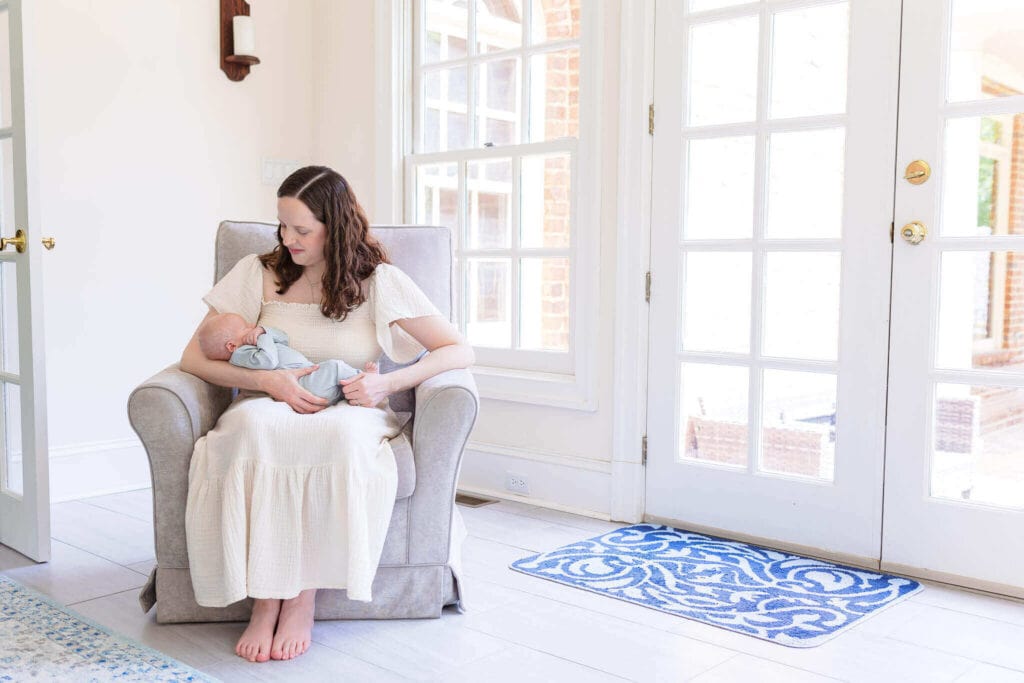 A mom sitting in a comfy chair in her home holding her baby boy during a lifestyle newborn session.