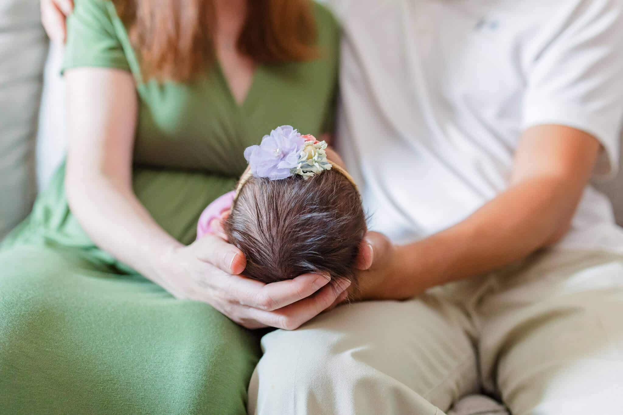 A close-up of a mom and dad sitting and holding their baby girl during a lifestyle newborn session in their home.