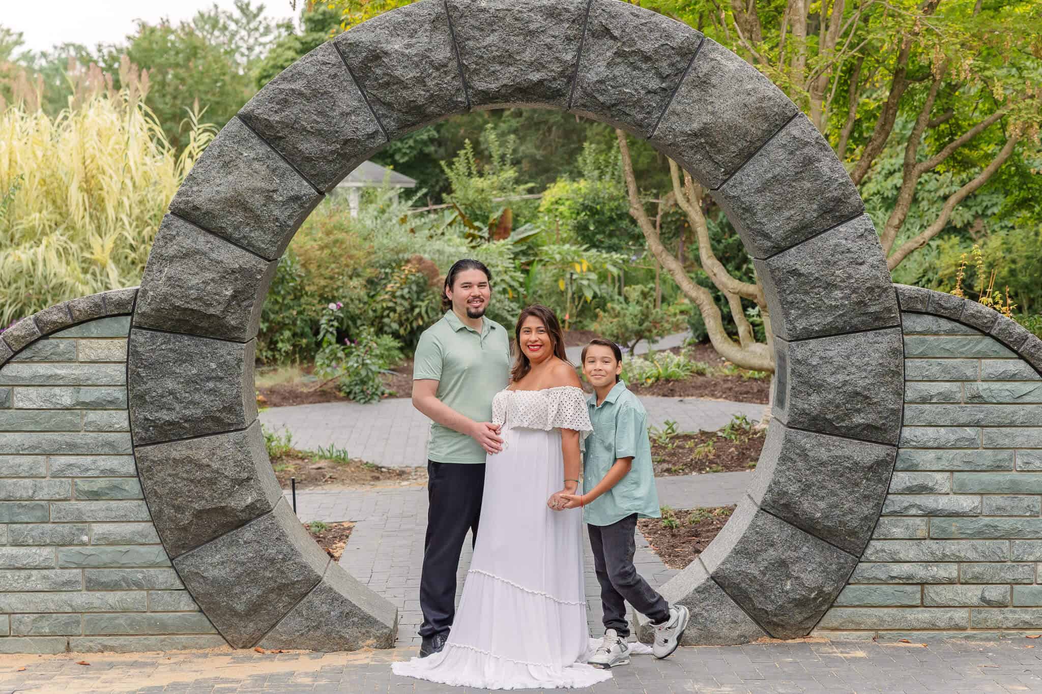 A pregnant couple and their older son posing in the Moon Gate at Green Spring Gardens, one of my favorite photoshoot locations in Northern Virginia.