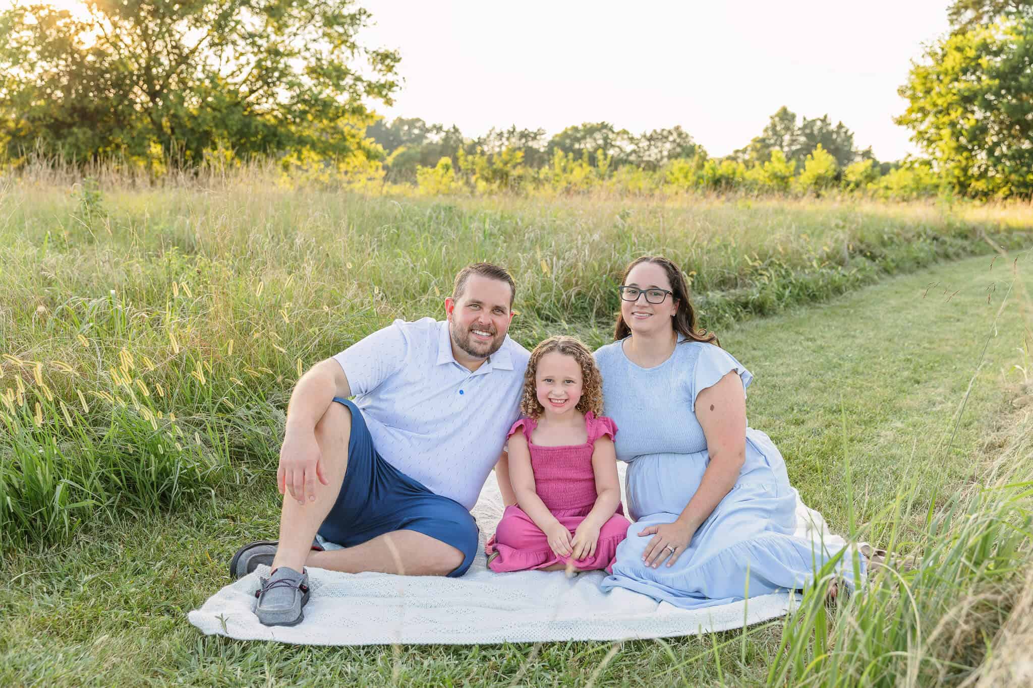A mom and dad sitting on a blanket with their daughter among the tall grass at Bristoe Station Battlefield, one of my favorite photoshoot locations in Northern Virginia.