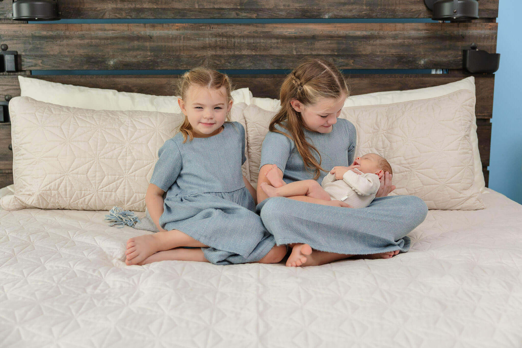 Two sisters sitting in bed and holding their baby brother during their in home newborn session.