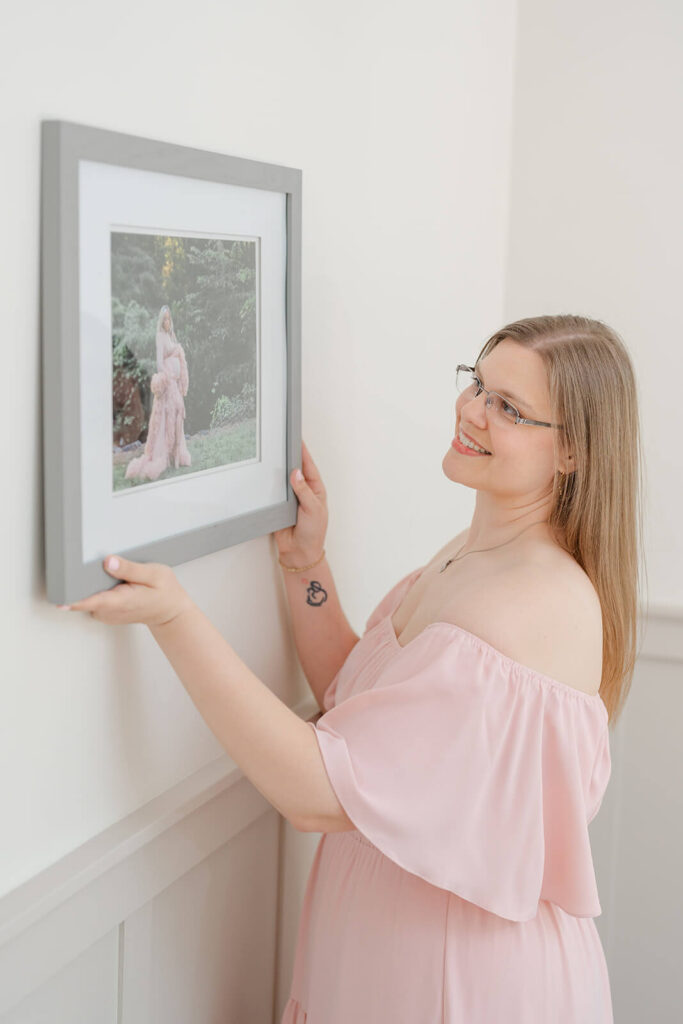 Photographer hanging a framed maternity print with a white mat