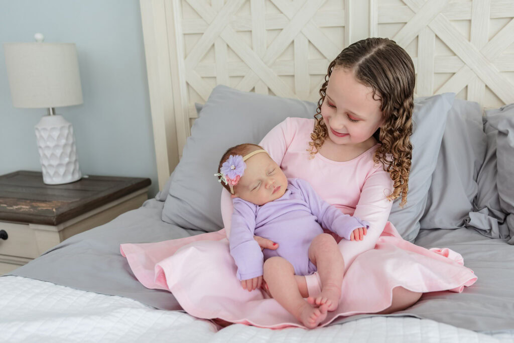 Big sister holding her baby sister on the bed during a lifestyle newborn session