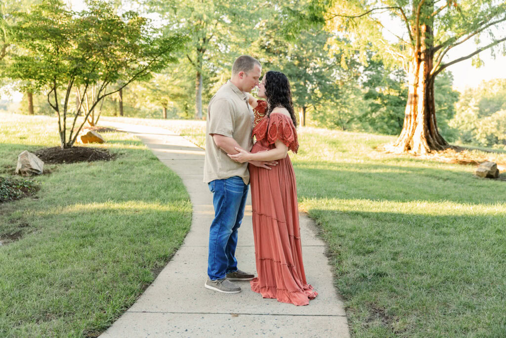 Expecting mom wearing a flowy rust off-the-shoulder dress for maternity photos in a park with her husband