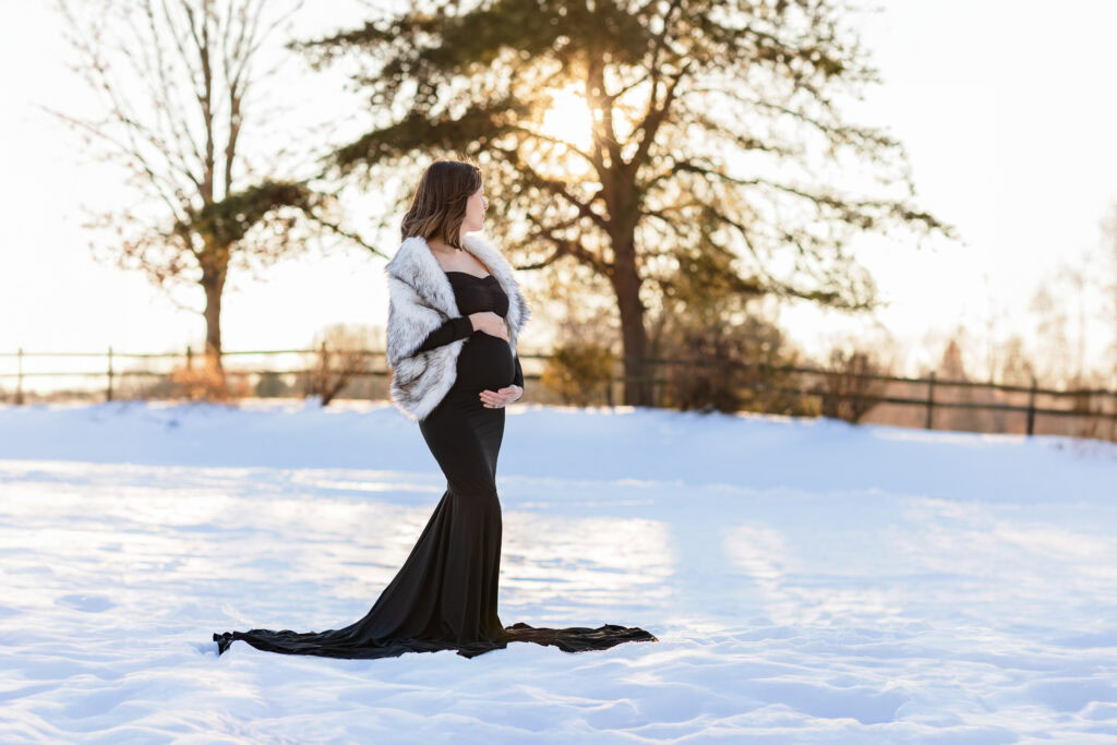 Pregnant mom in a black dress and fur shrug during a snowy winter maternity session